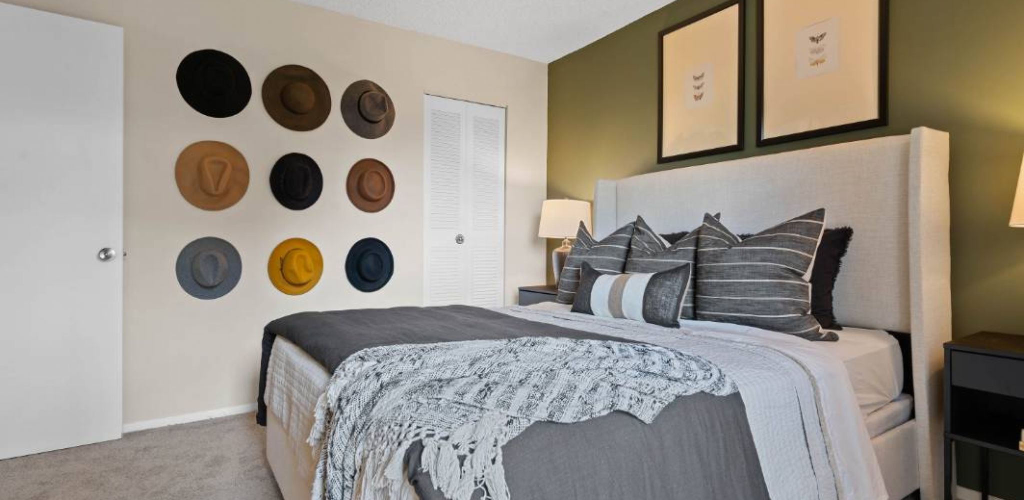 Hawthorne at Southside apartment bedroom with a neatly made bed, a stylish dresser, and a unique wall adorned with an assortment of hats